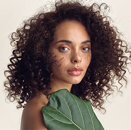woman with curly long hair with a big green leaf over her shoulder